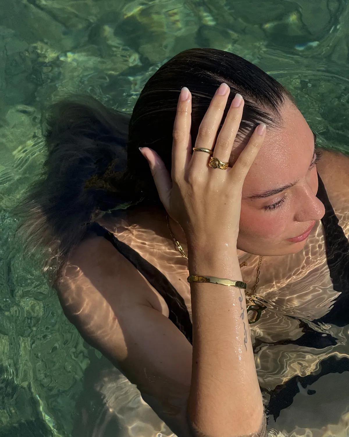 Mujer dentro del mar con anillos, pulsera y collares de baño de oro 18 k puestos